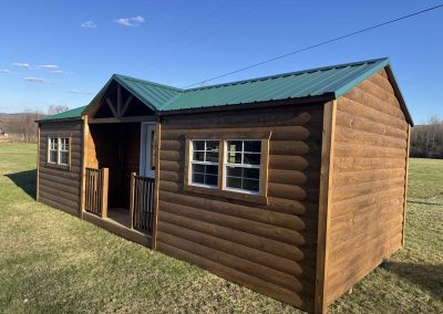 Amish cabin with green roof, dark wood siding and covered porch