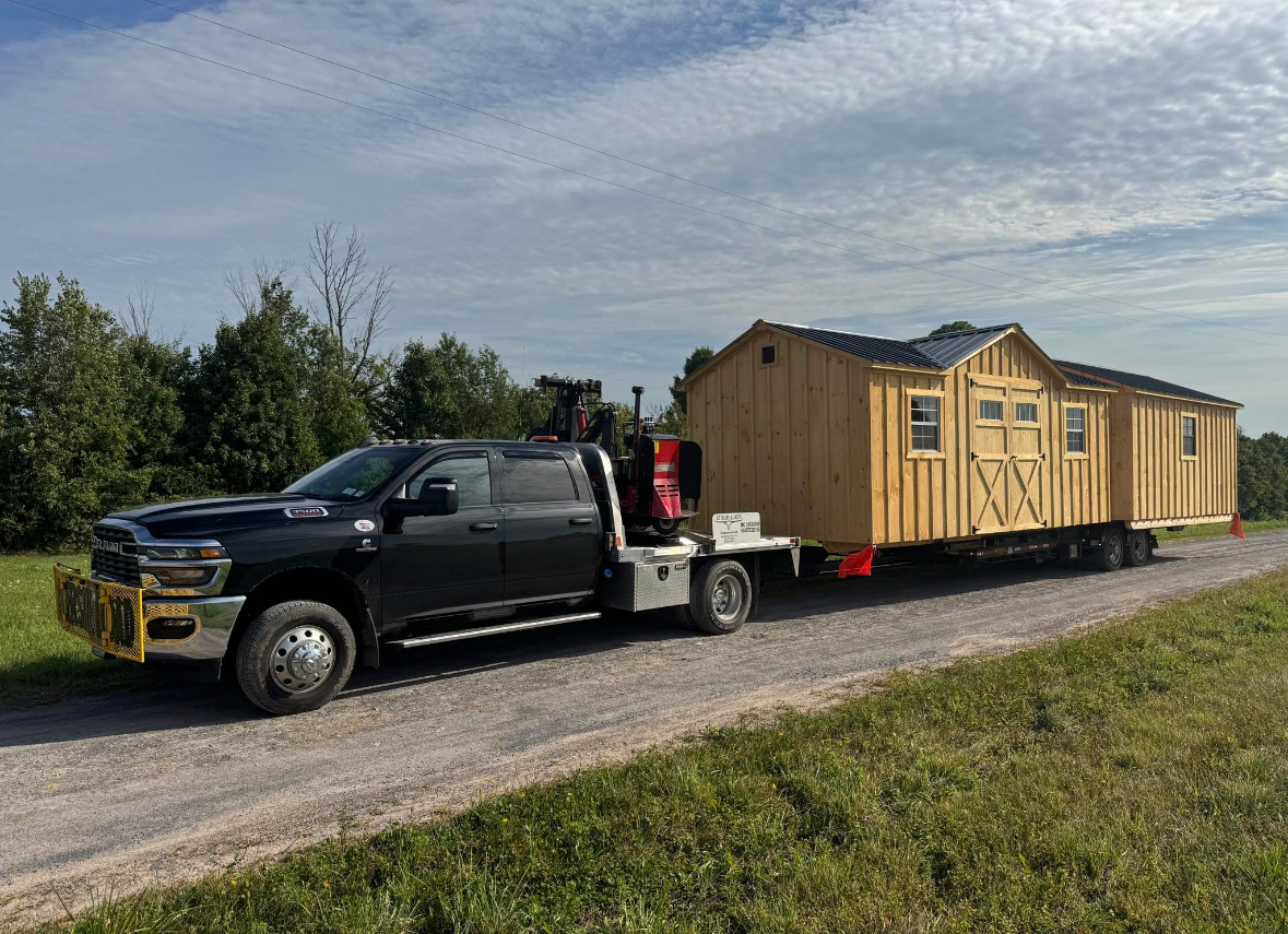 Black St Mary & Sons Truck with a shed on a trailer being dropped off onto grass