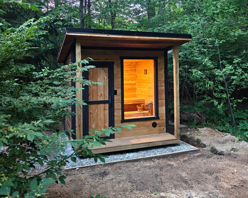 Stunning wood sauna with black trim surrounded by trees